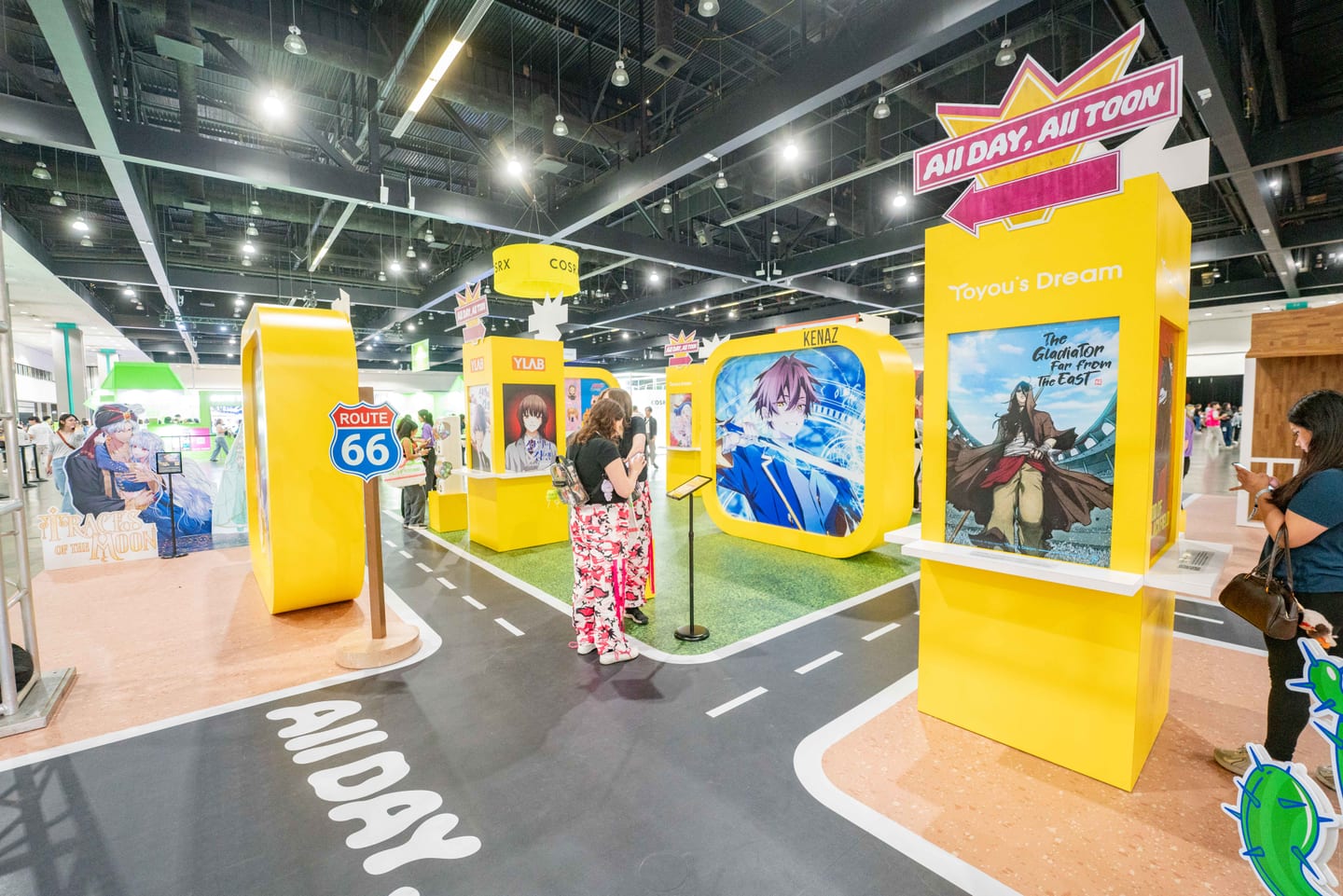 The yellow All Day All Toon webtoon activation at KCON LA 2025, built as a Route 66 road with illustrated series panels along it