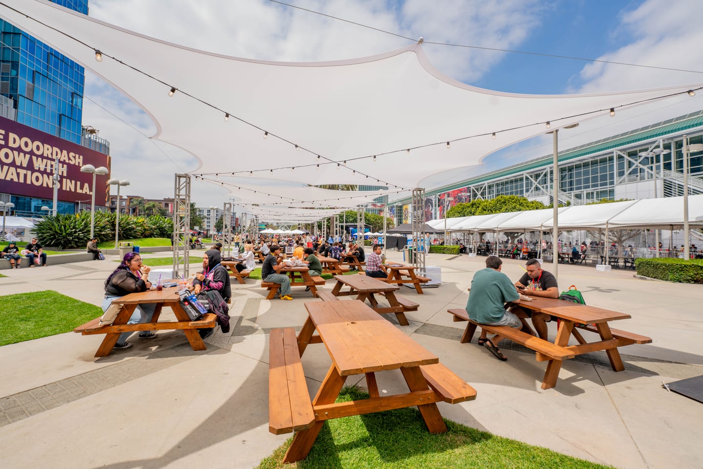 Attendees resting at picnic tables under string lights in the DoorDash-branded outdoor lounge at Anime Expo 2026