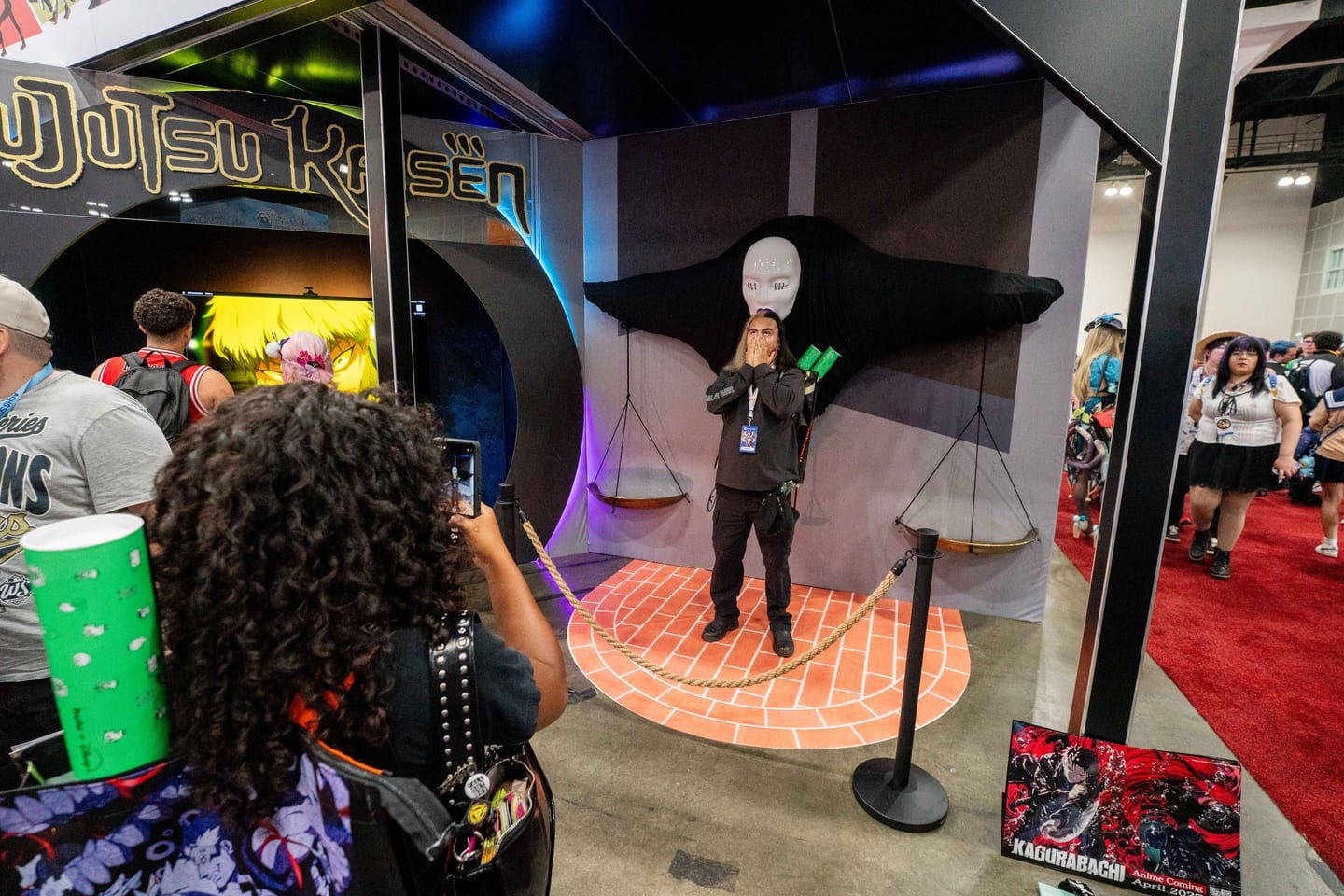 An attendee photographing a costumed performer at the Jujutsu Kaisen experiential photo activation at Anime Expo