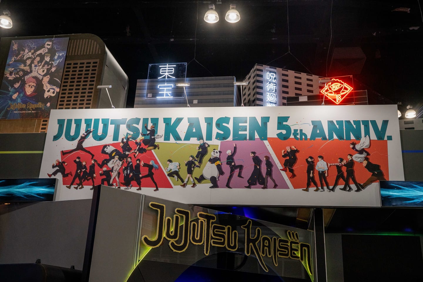 A large Jujutsu Kaisen 5th Anniversary exhibitor booth with a cityscape set and neon signage at Anime Expo