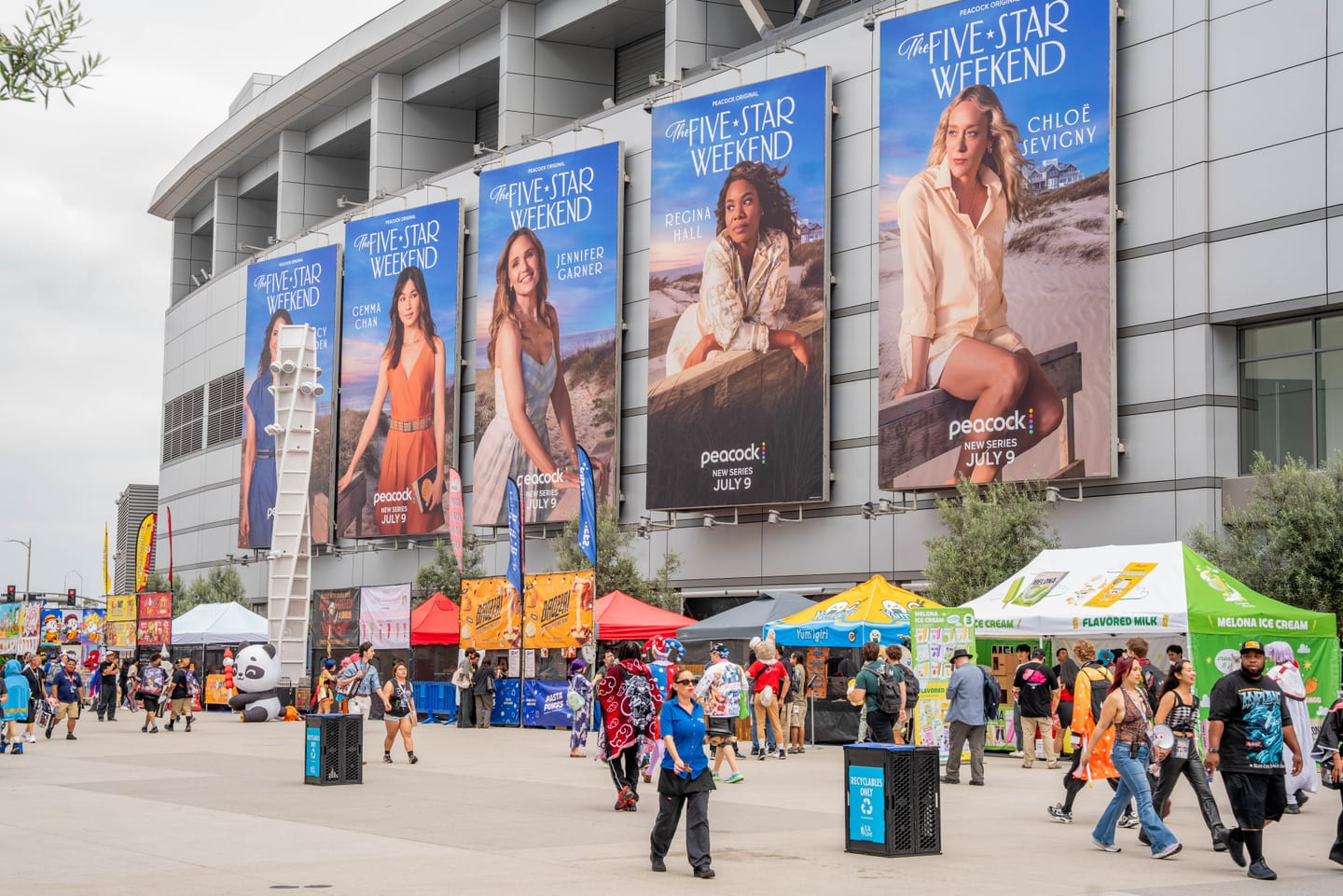 Giant Peacock banners for the series The Five-Star Weekend, featuring Chloë Sevigny and Jennifer Garner, wrapping the arena facade above the Anime Expo 2026 outdoor food village