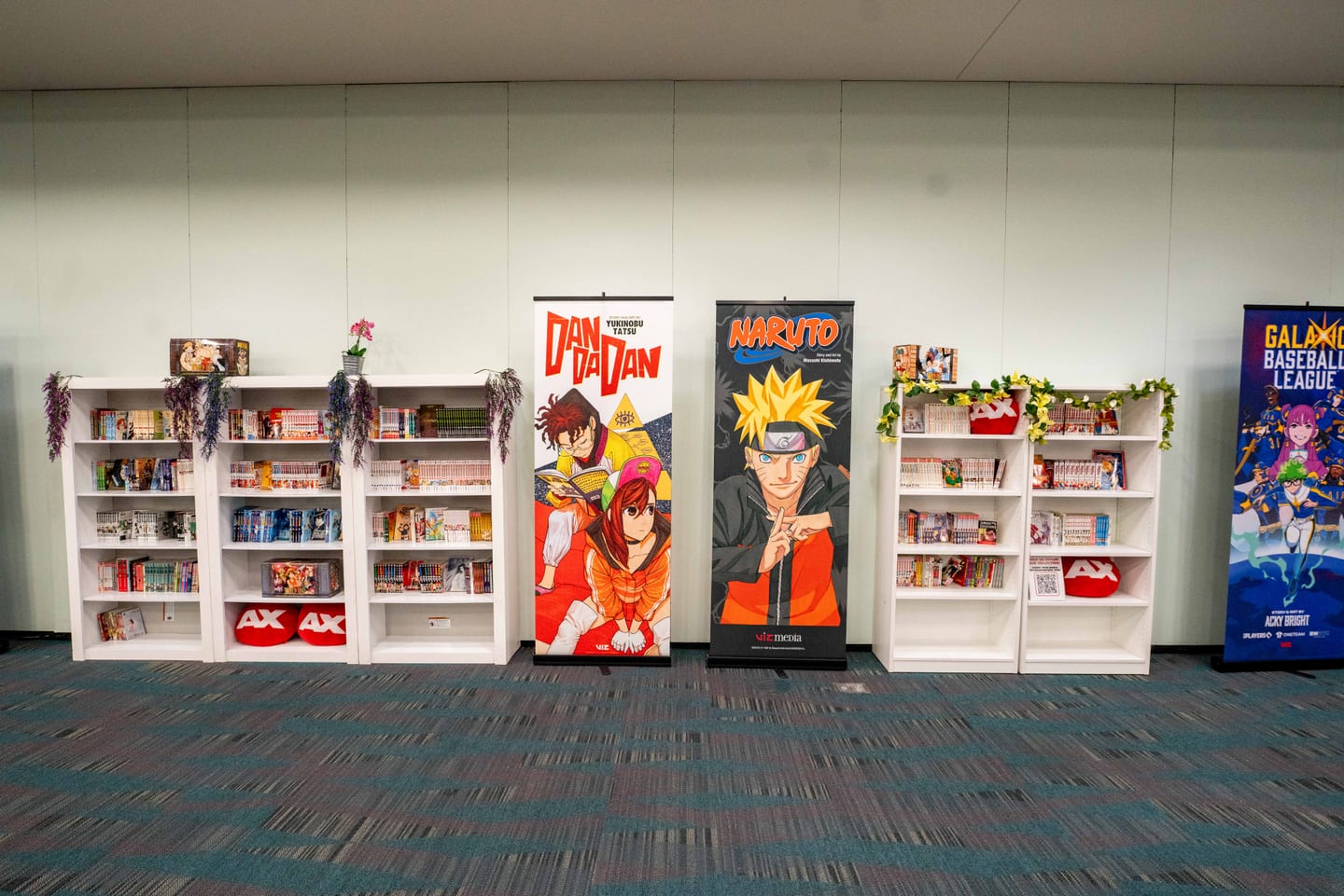 A quiet AX reading lounge stocked with manga, with VIZ Media banners for Naruto and Dandadan flanking the shelves at Anime Expo 2026
