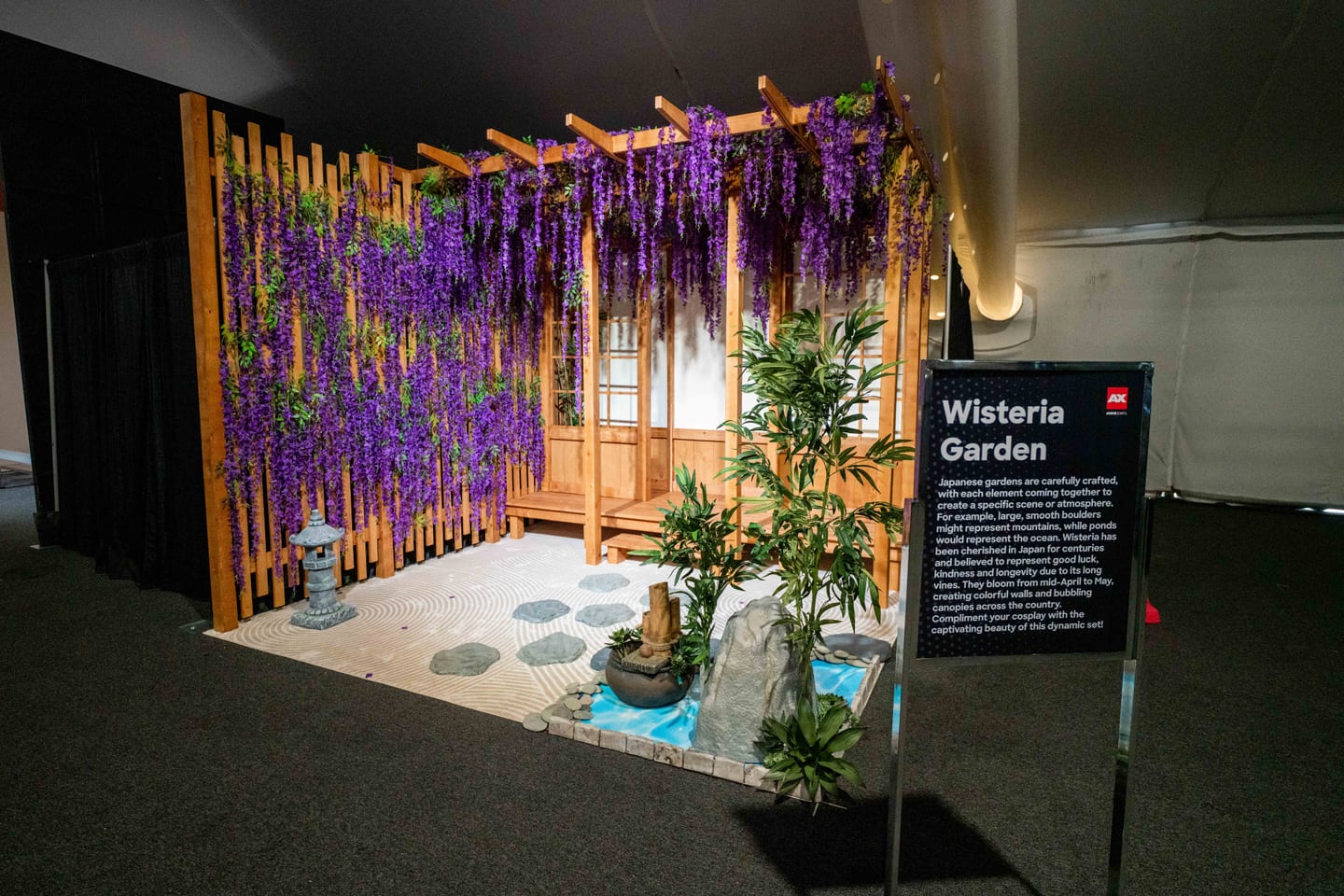 A calm Wisteria Garden lounge installation with hanging purple wisteria and a zen wooden path at Anime Expo 2026