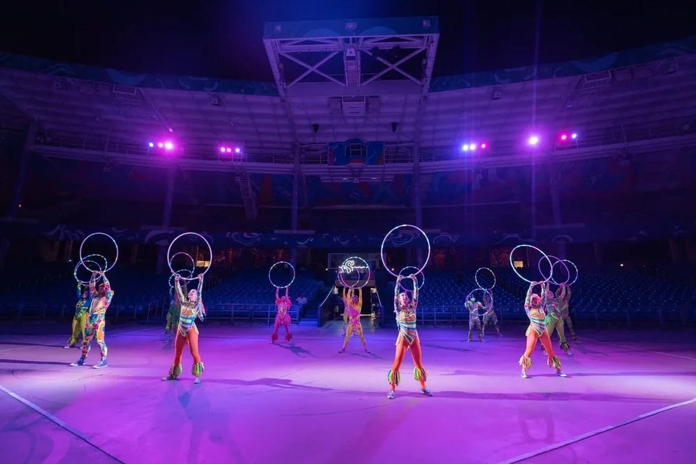 Performers spinning illuminated hoops on the arena floor under purple stage lighting at a corporate live show