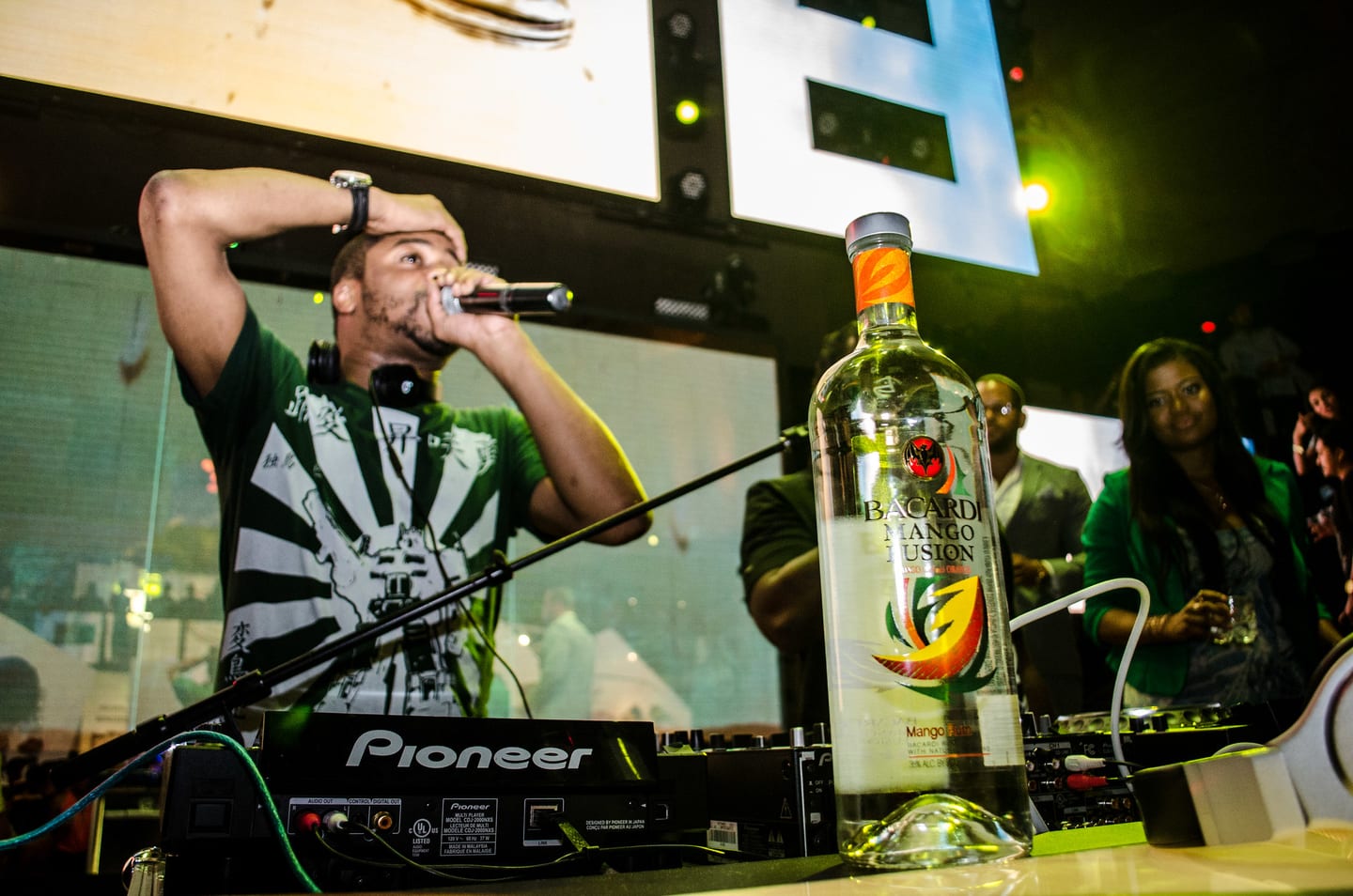 A host on the mic behind a DJ booth with a Bacardi Mango Fusion bottle at a nightlife brand launch in Hollywood