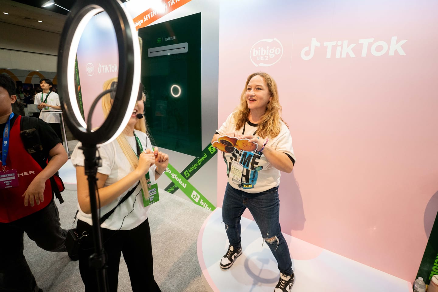 A creator being filmed with a ring light in front of a co-branded bibigo and TikTok backdrop at KCON LA 2025