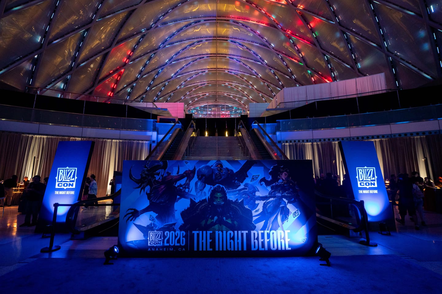 A lit BlizzCon 2026 The Night Before backdrop with Blizzard game art, flanked by BlizzCon banners under the ARTIC roof