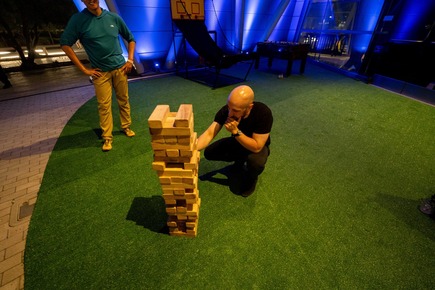 A guest crouching to pull a block from a giant Jenga tower on a patch of lawn outside ARTIC
