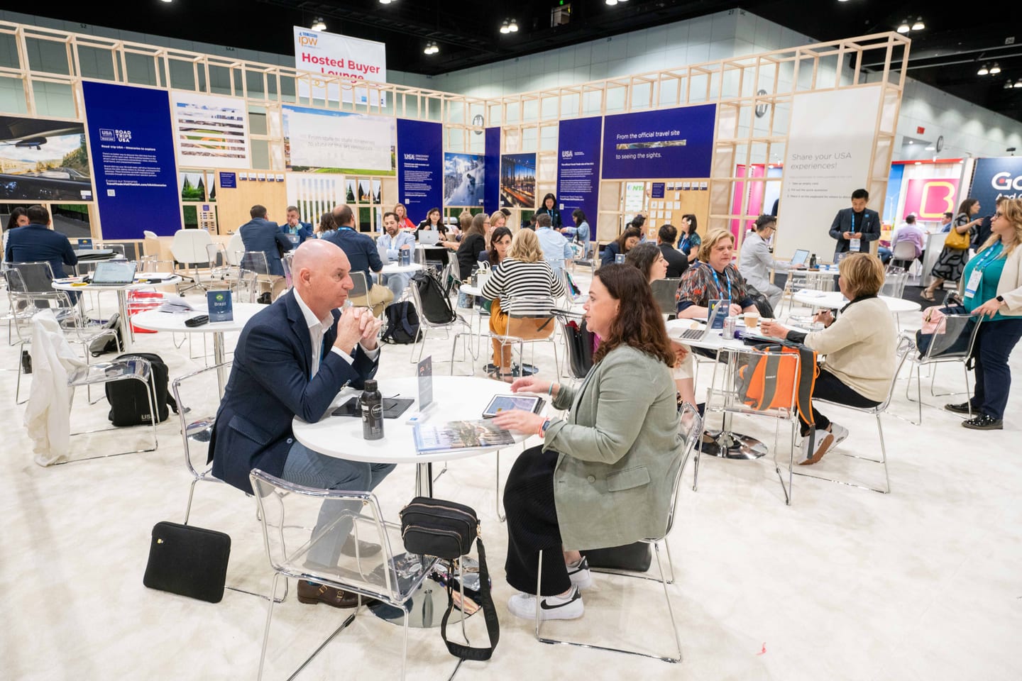Delegates meeting in a lounge area among destination stands on the Brand USA Marketplace floor at IPW
