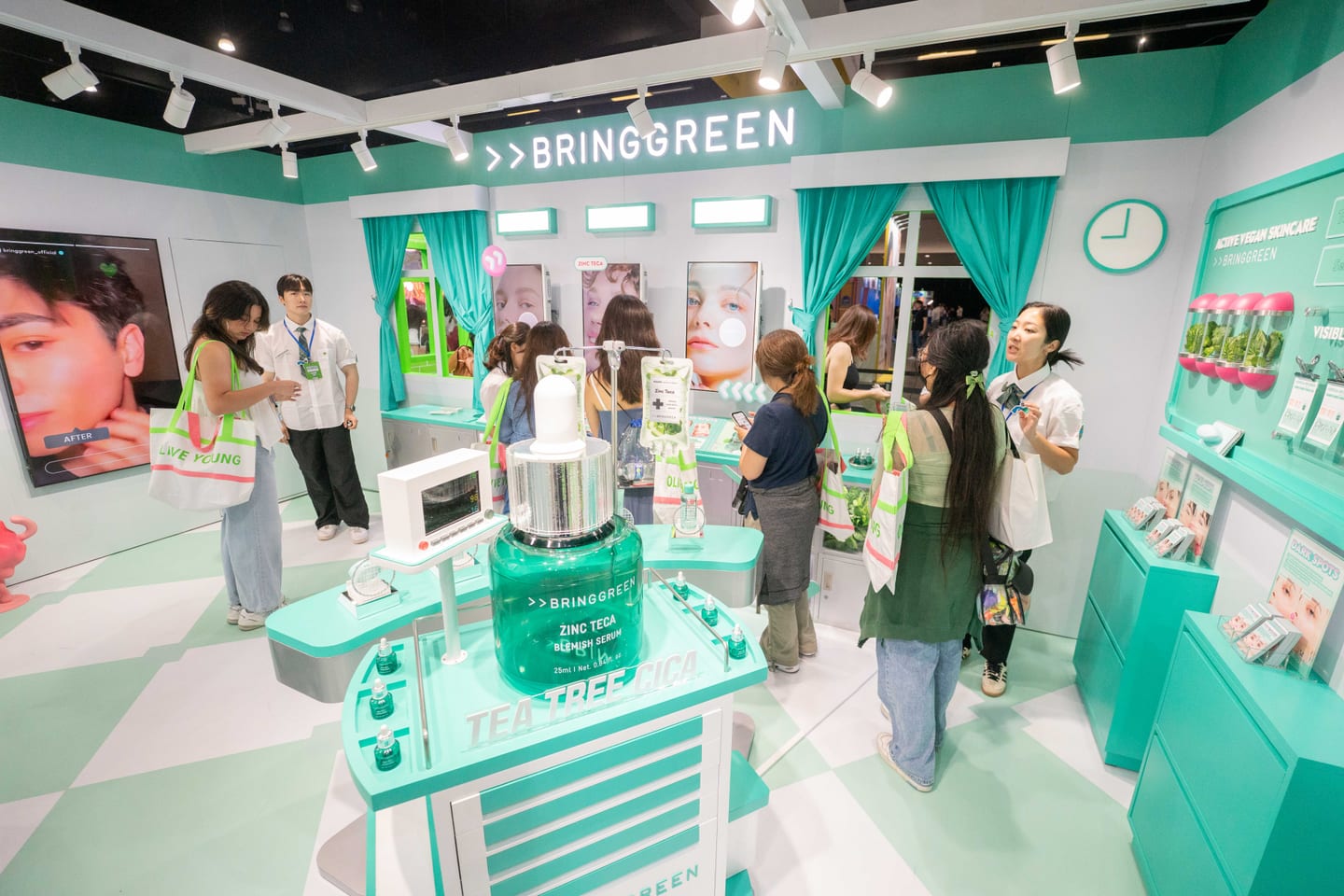 The mint-green Bring Green skincare booth at KCON LA 2025 with a giant Tea Tree Cica toner bottle and staff running product demos