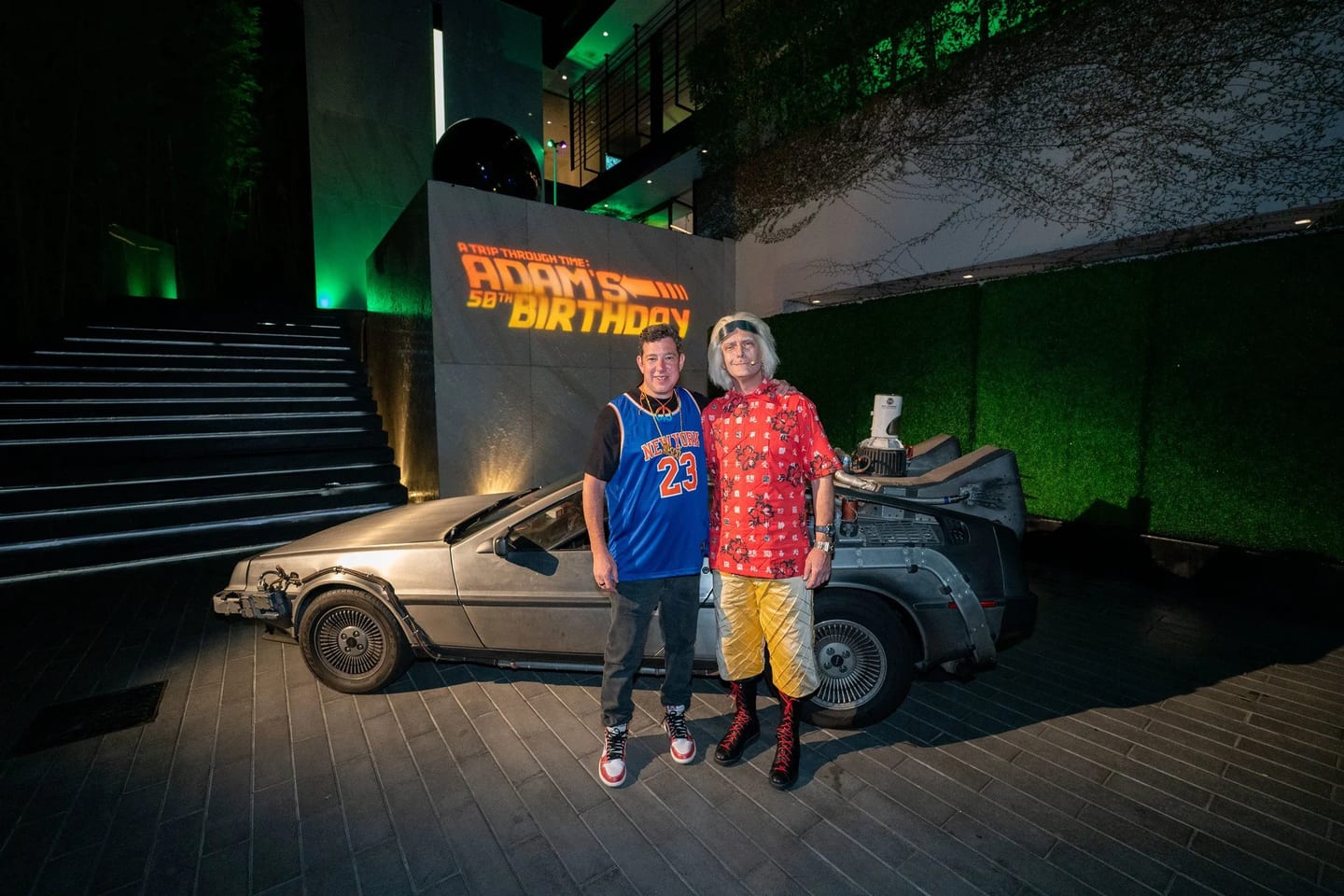 Two guests posing with a DeLorean at a Back to the Future themed 50th birthday party