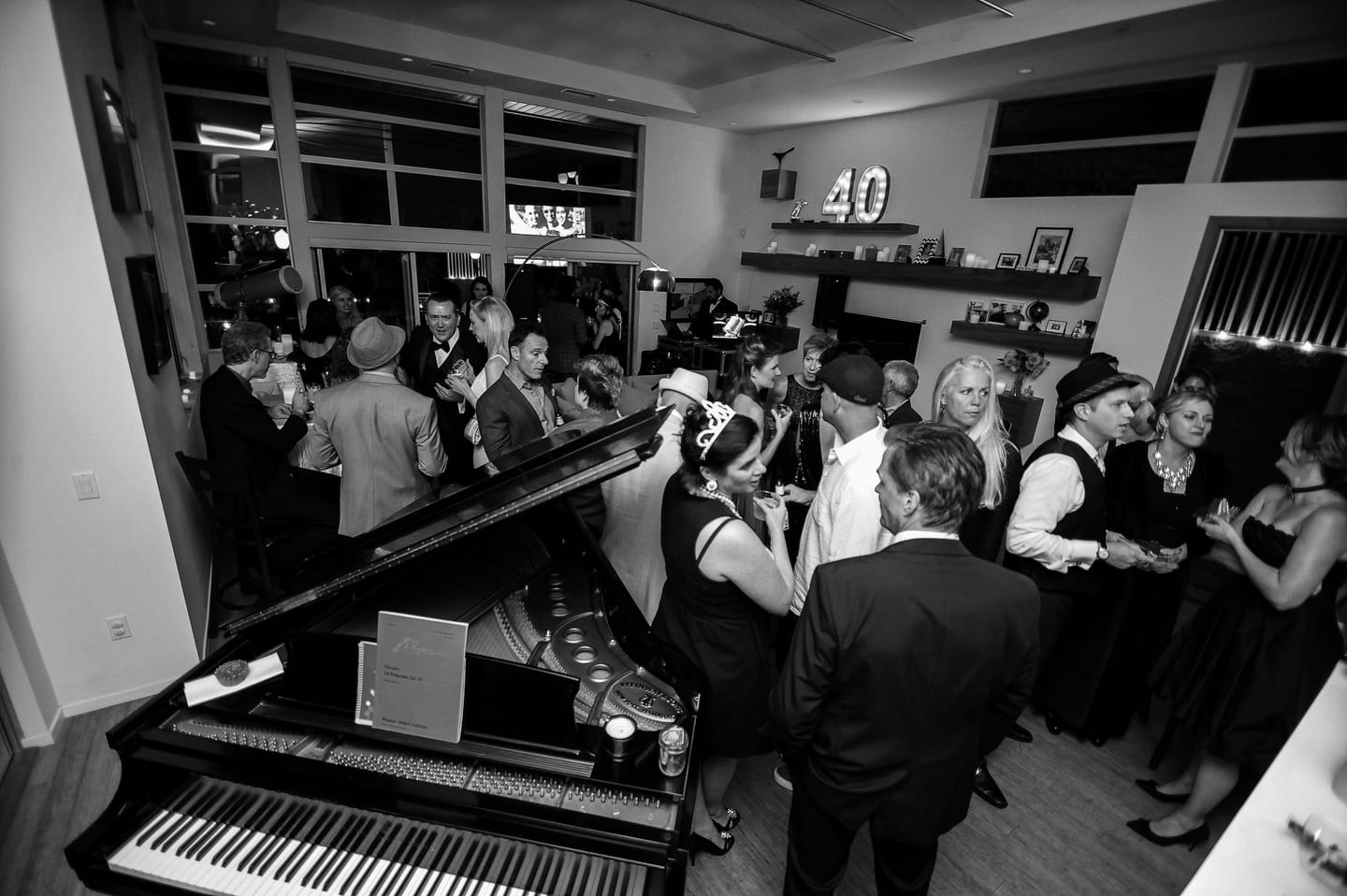Black-and-white photo of guests at a 40th birthday party with a grand piano in the foreground