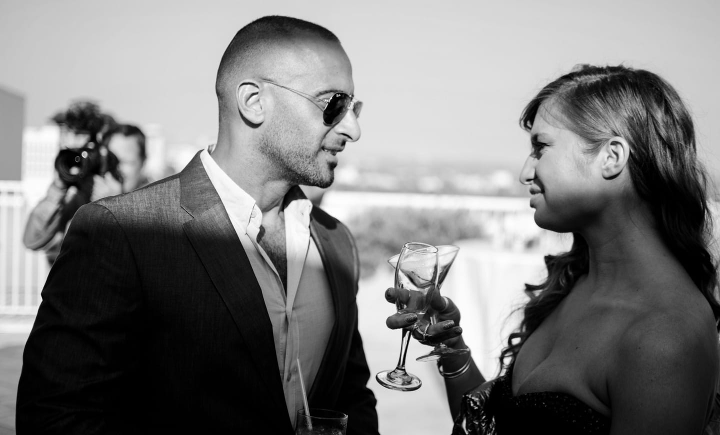 Black-and-white photo of a guest in sunglasses holding a champagne glass at a rooftop party