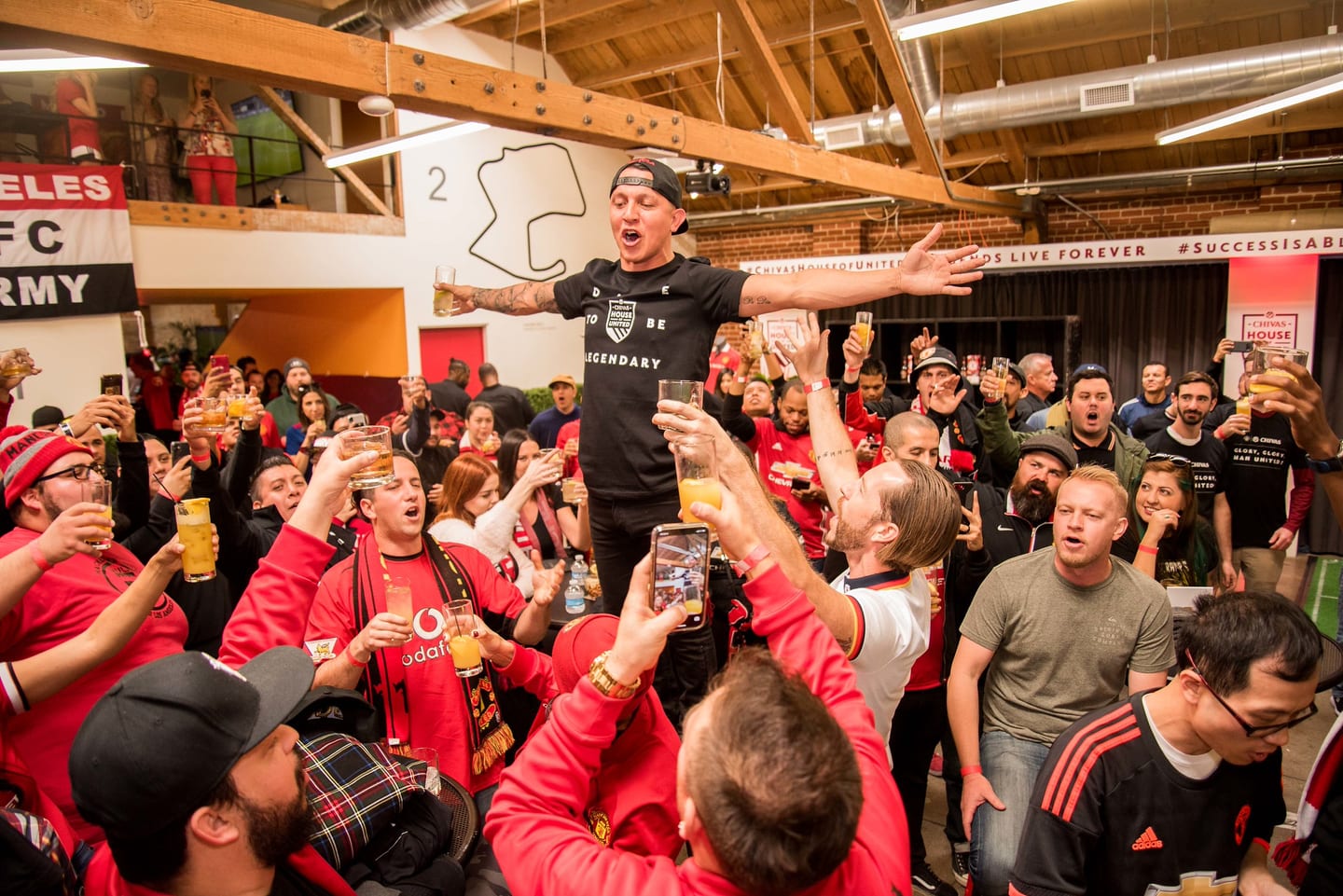 A crowd of Manchester United fans in red raising glasses in a toast at the Chivas House of United watch party in Los Angeles