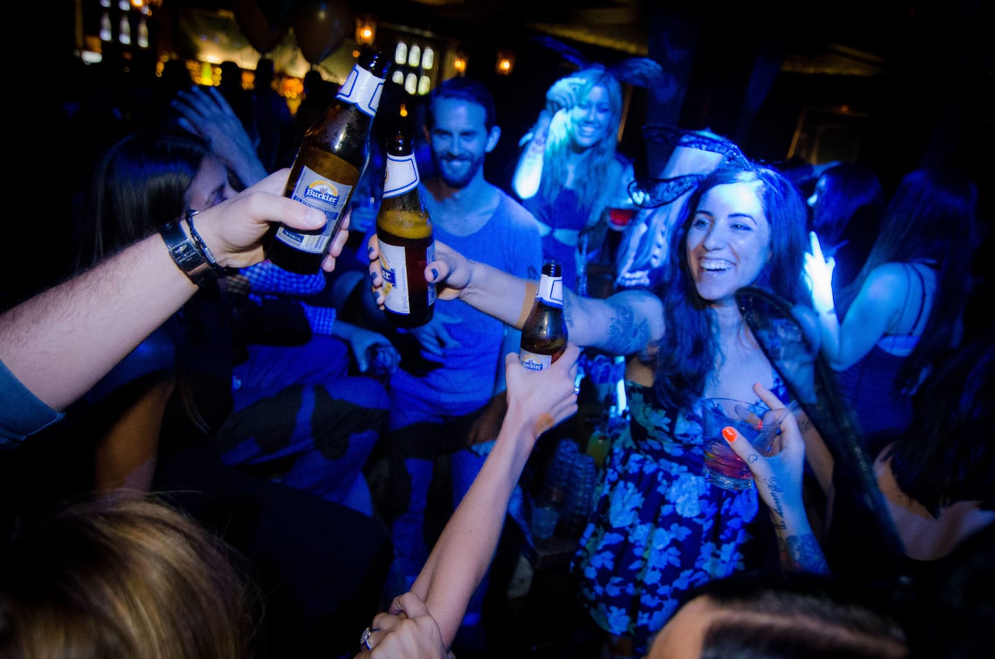 Friends toasting with bottles on a nightclub dancefloor in blue light