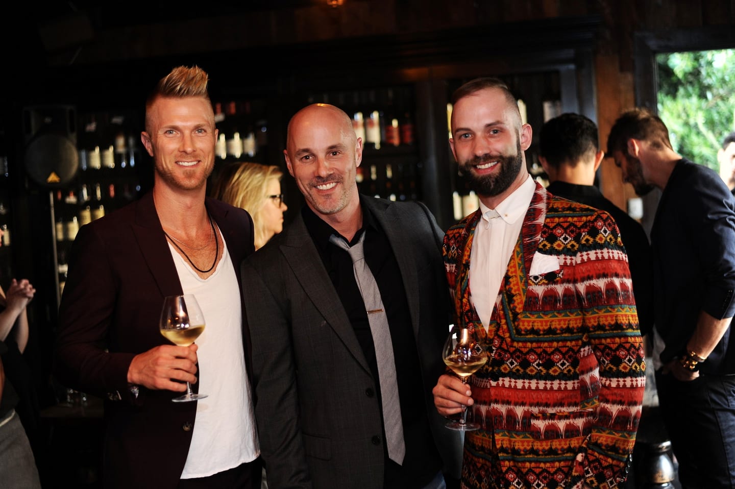 Three guests in jackets with wine glasses at a cocktail party