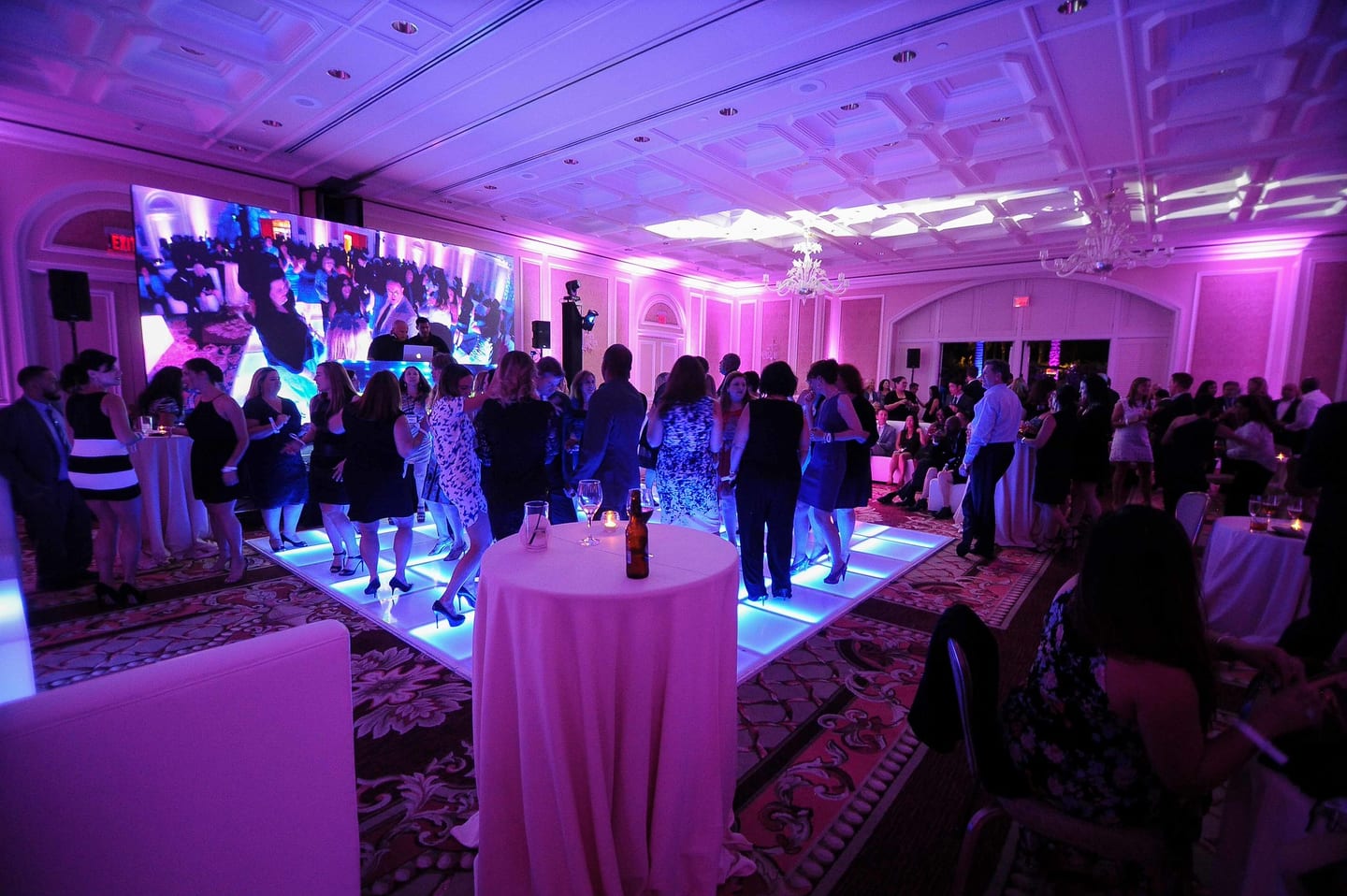 Guests mingling in a pink-lit hotel ballroom with a lounge runner down the center
