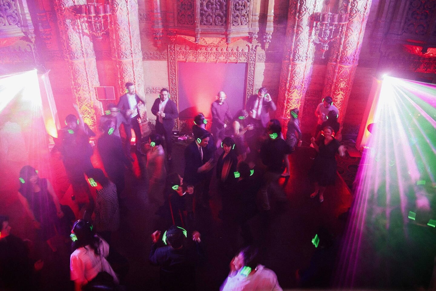 Crowd dancing in an ornate theater venue washed in pink light