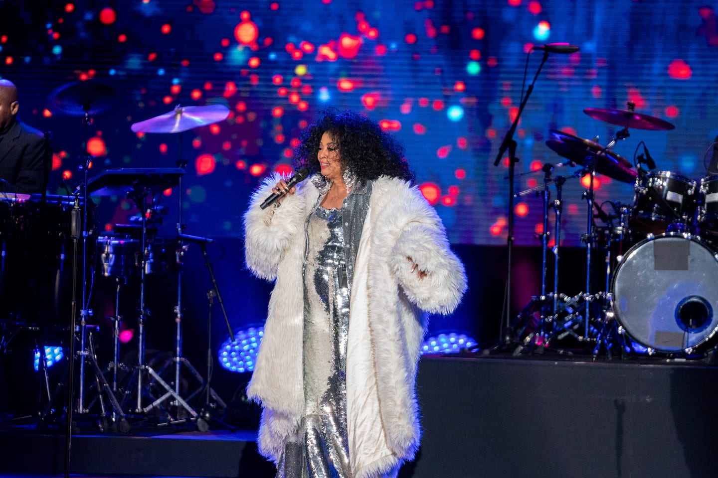 Diana Ross singing in a white fur coat under blue and red stage light at the IPW opening at the L.A. Coliseum
