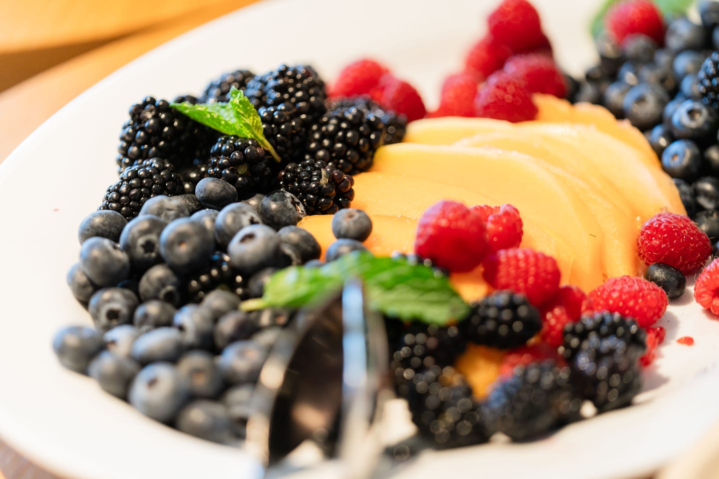 A plate of blackberries, blueberries, raspberries, and sliced melon garnished with mint