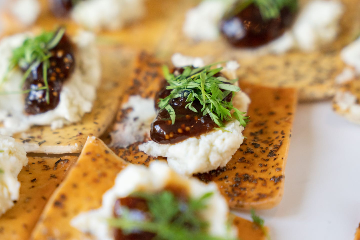 Close-up of a canapé — goat cheese and fig jam on a seeded cracker topped with fresh herbs