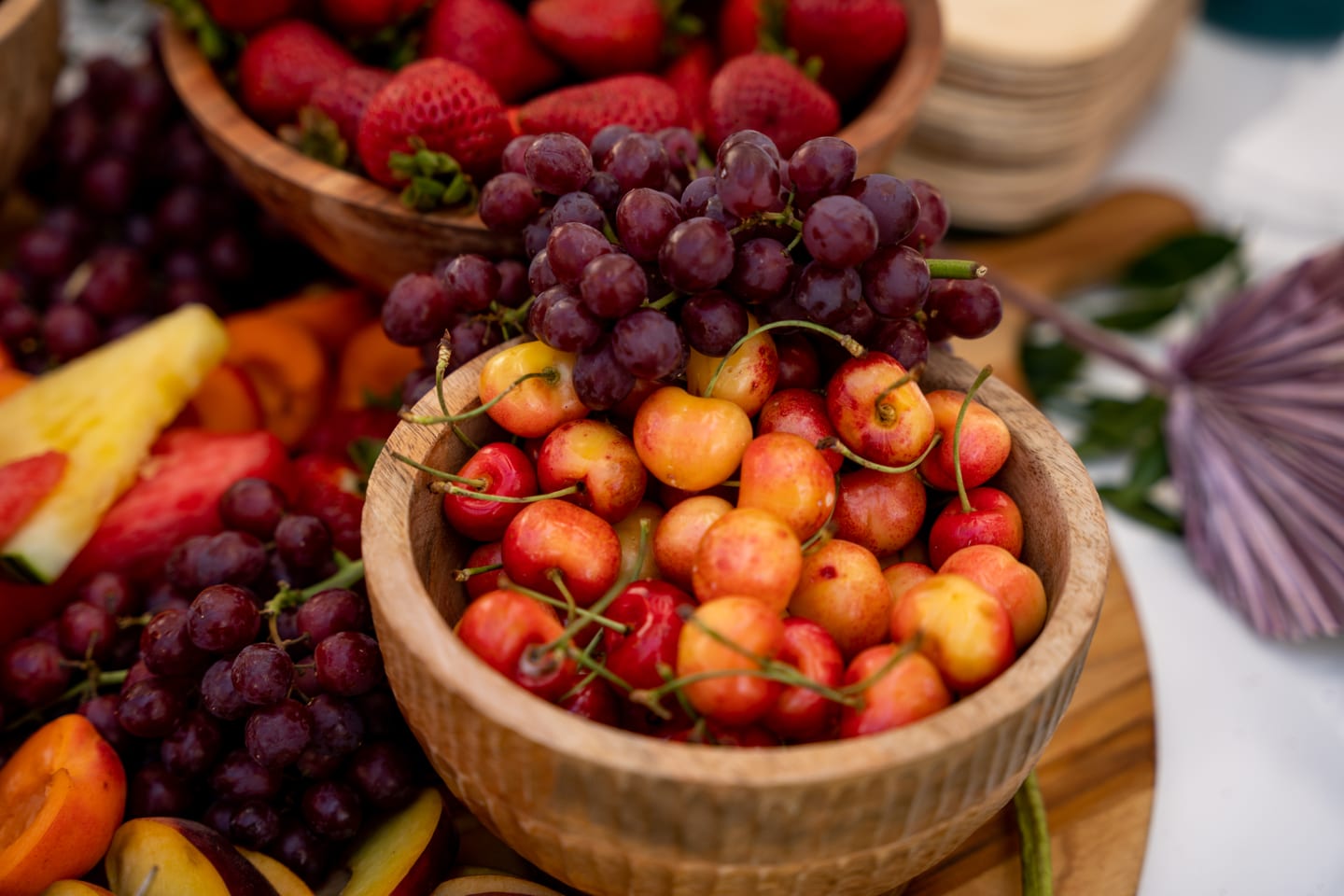 Carved wooden bowls of cherries, red grapes, and stone fruit styled on a buffet
