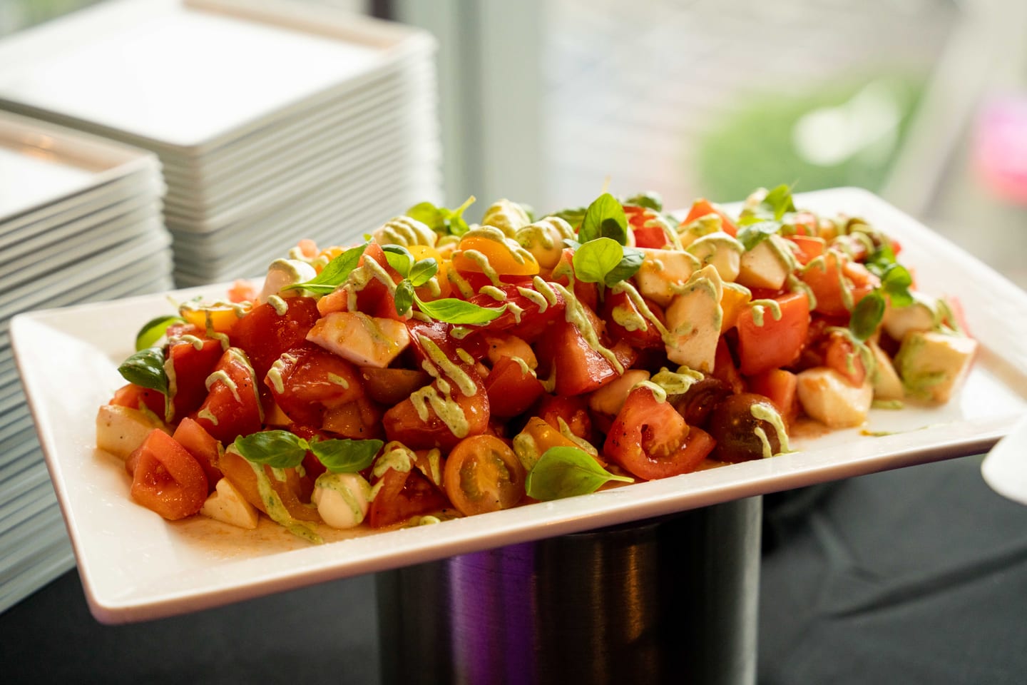 A platter of heirloom tomato and mozzarella salad with basil and green dressing on a buffet