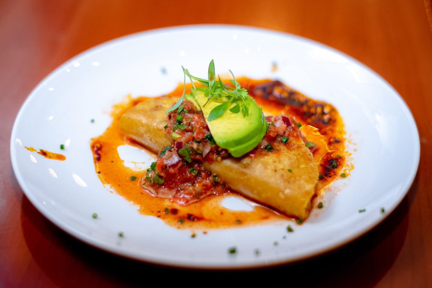 A plated empanada with tomato salsa, avocado, and chili oil on a white plate