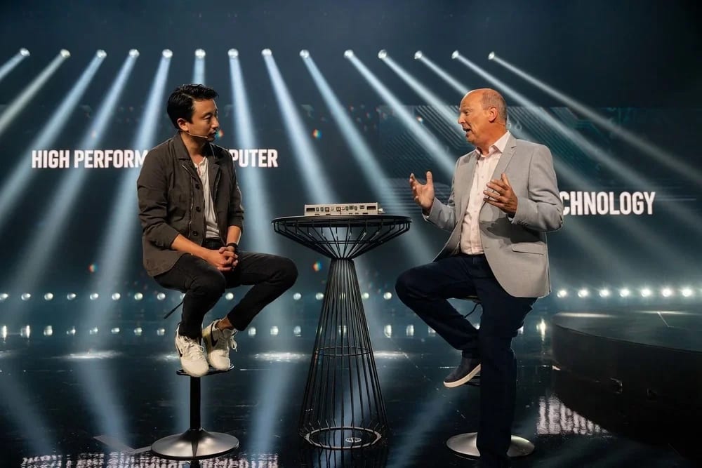 Two speakers in conversation on stools under white light beams on stage at the Fisker auto reveal
