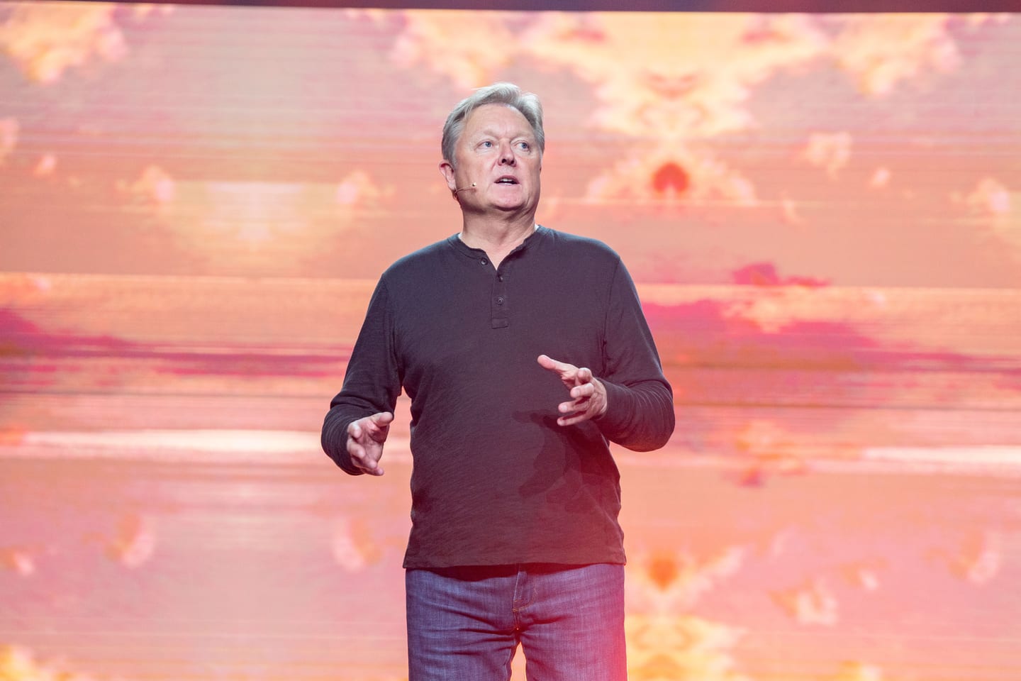 A presenter mid-remark against the sunrise sky screen