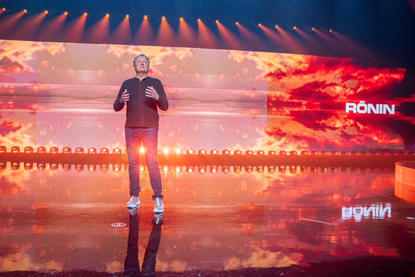 A speaker on stage against the fiery orange RONIN screen