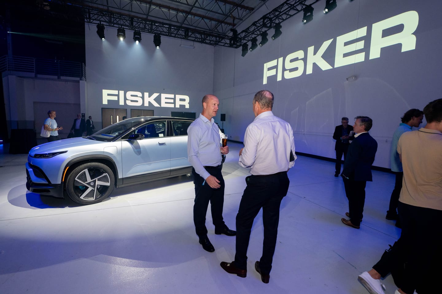 Guests talking beside a pale blue Fisker Ocean beneath FISKER wordmarks