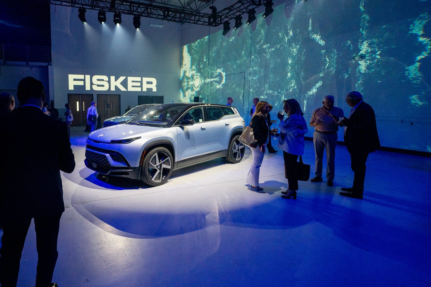 Guests gathered around a white Fisker Ocean beneath the projected FISKER wall
