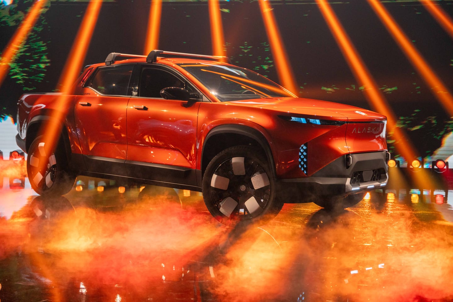 The orange Fisker Alaska pickup on stage in fog under orange light beams