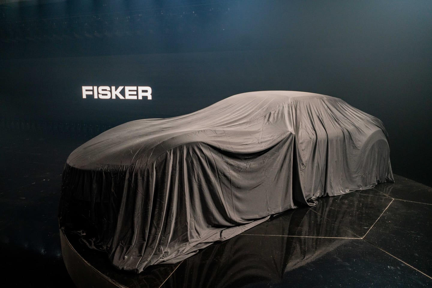 A covered vehicle beside the glowing FISKER wordmark before the reveal
