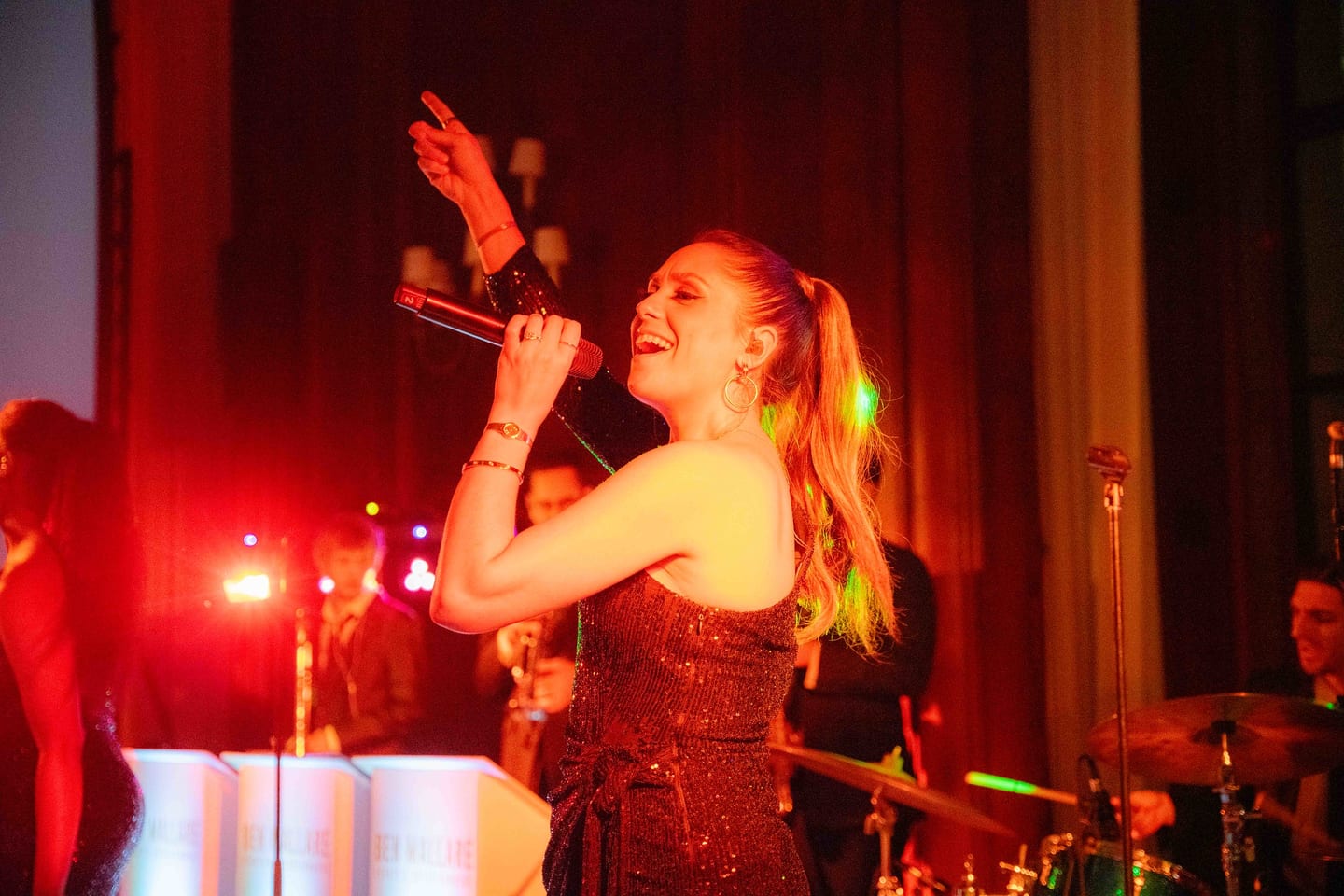 Singer performing with a live band under red light at a gala