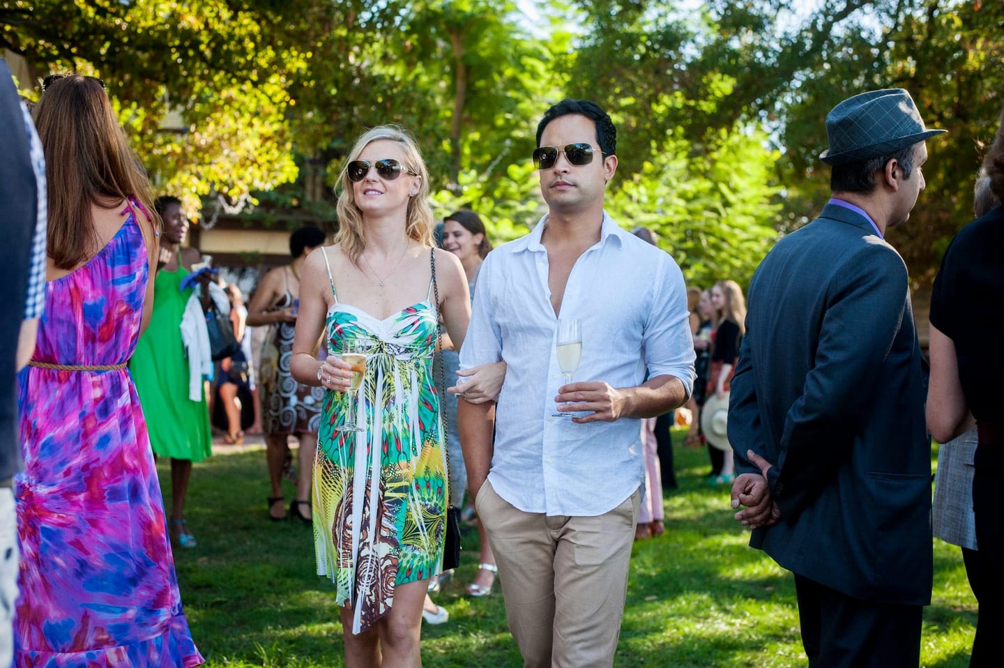 Guests walking through a sunlit garden with drinks at an outdoor private party