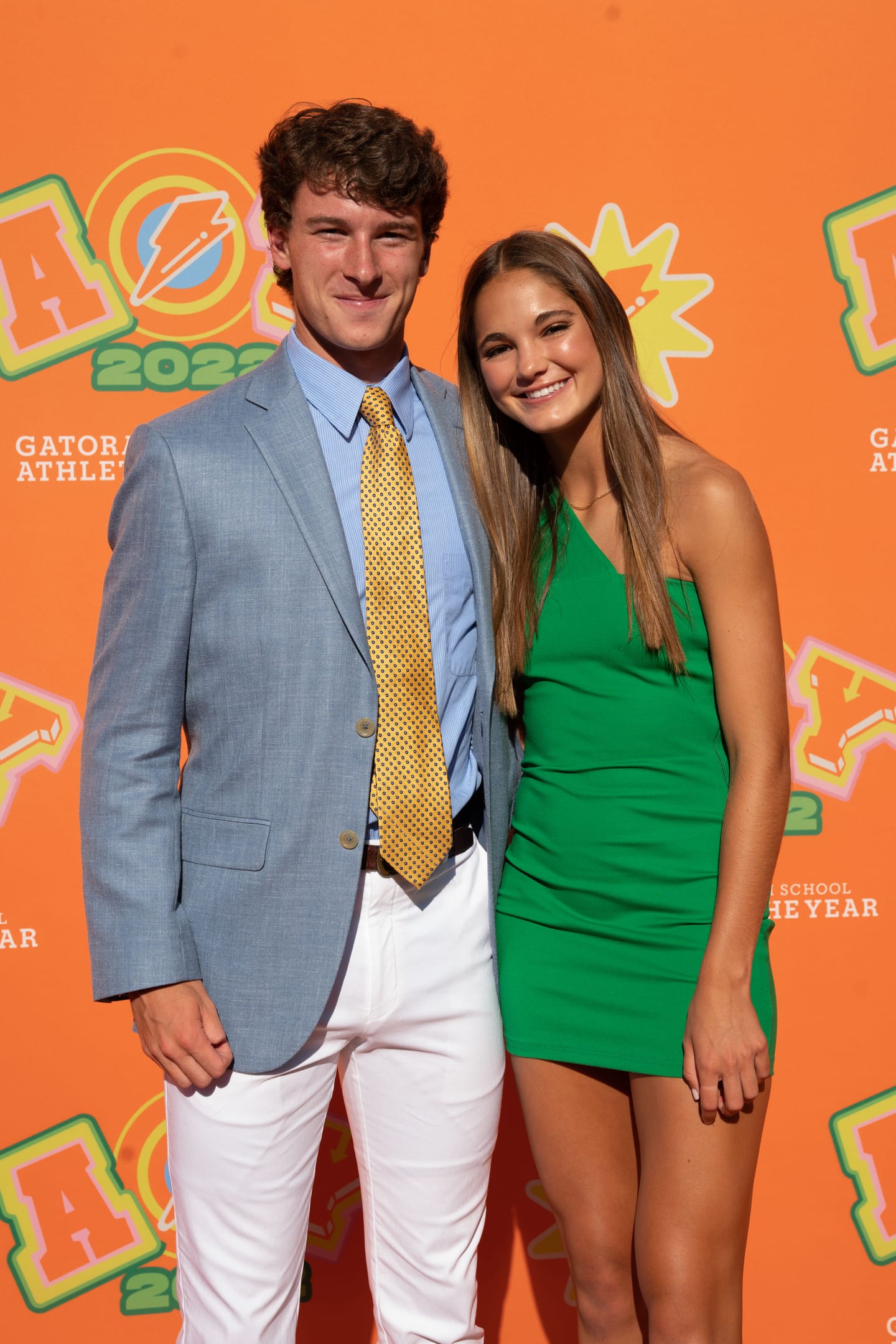 A couple photographed together against the orange AOY 2022 step-and-repeat