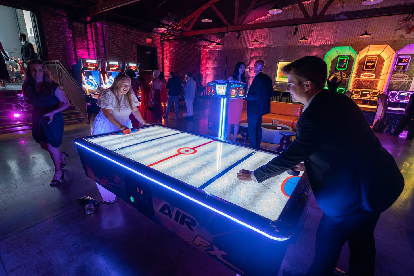Guests playing air hockey on a lit table on the arcade floor