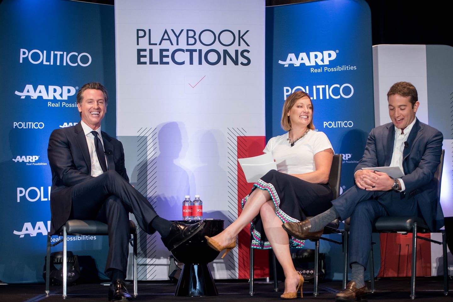 Gavin Newsom laughing on stage during a Politico Playbook Elections panel with AARP branding