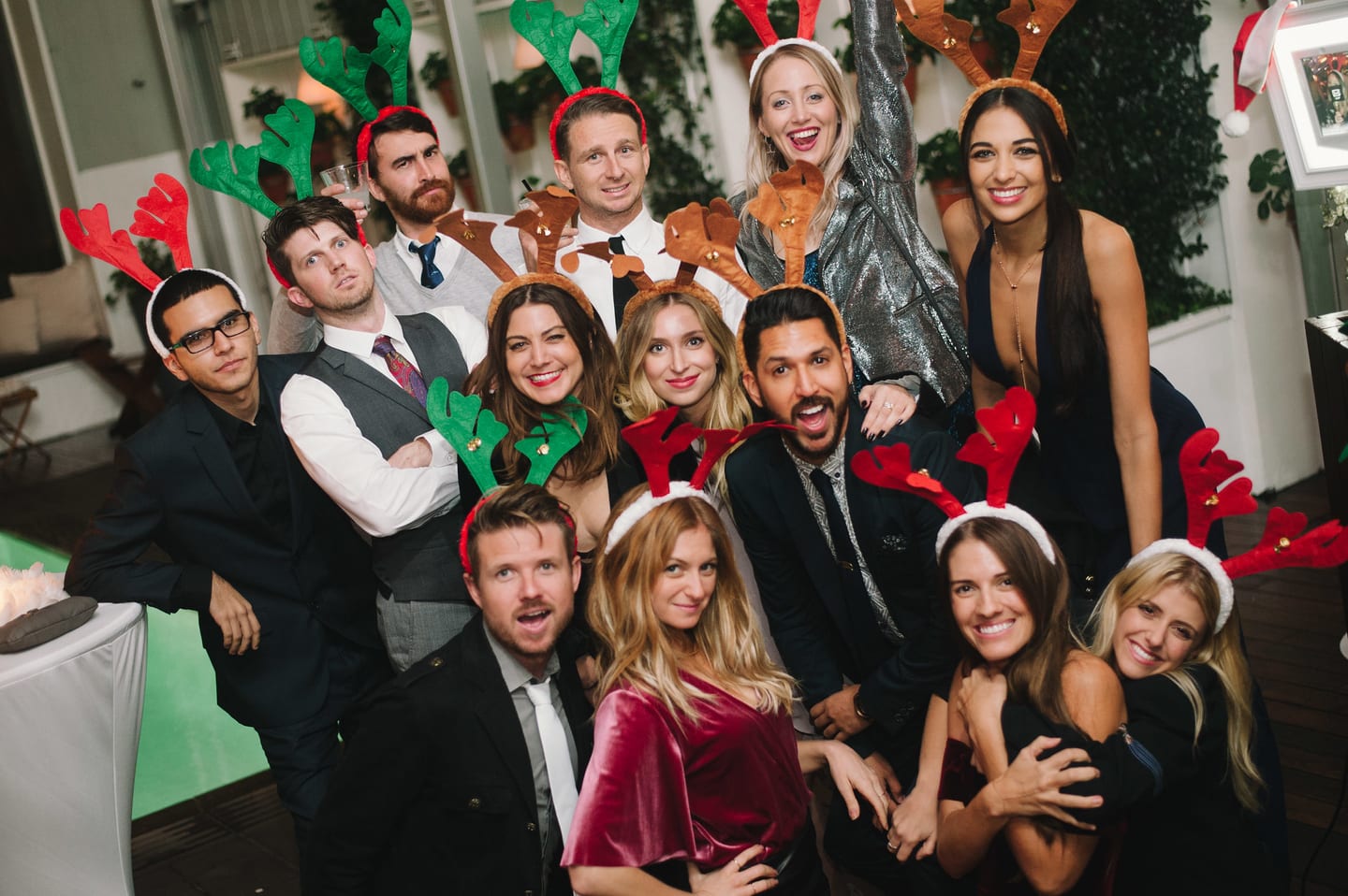 A group in reindeer antlers and holiday hats crowded together in a green-screen photo booth