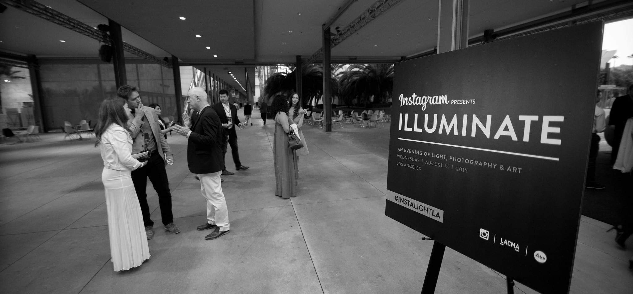 Black-and-white wide view of guests mingling in the plaza beside the Instagram Illuminate signage at LACMA, an evening of light, photography and art in Los Angeles