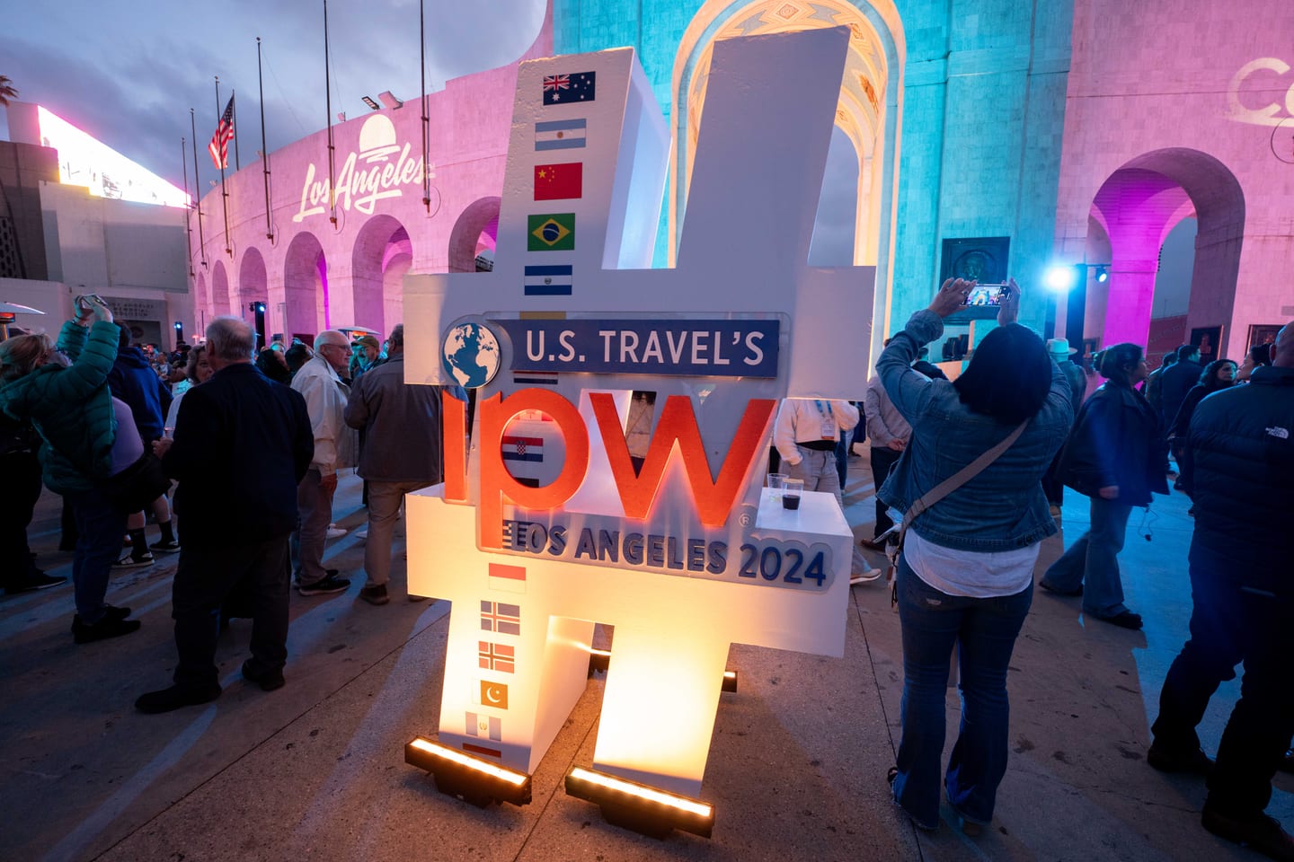 Illuminated U.S. Travel IPW Los Angeles 2024 marquee letters at night with delegates gathered around them