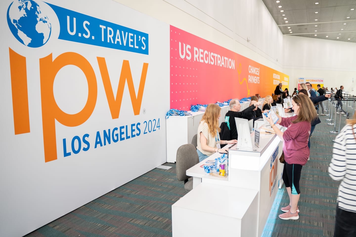 A long U.S. Registration desk staffed along a wall printed with the U.S. Travel IPW Los Angeles 2024 logo as delegates check in