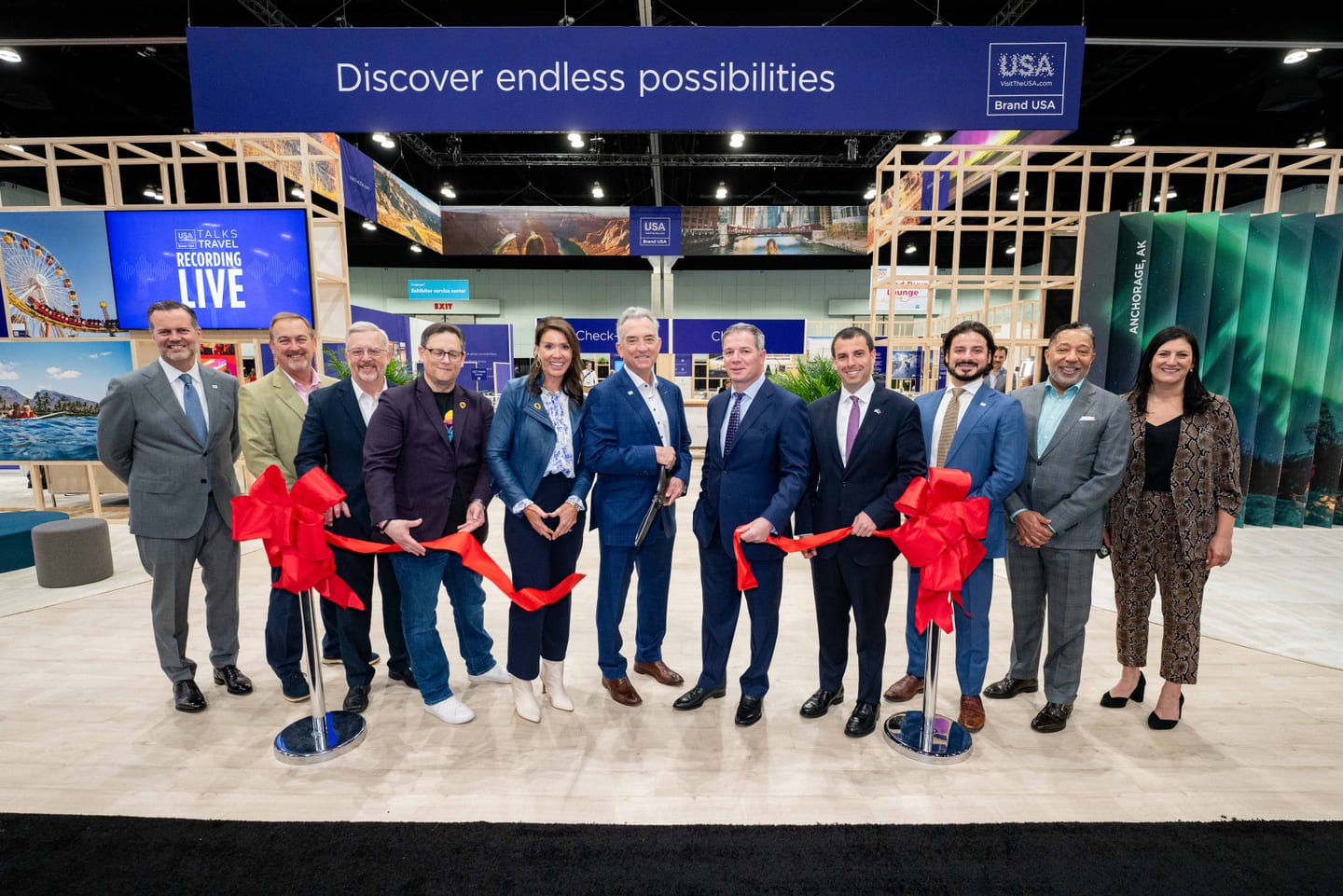 A line of travel-industry executives cutting a red ribbon to open the IPW Marketplace beneath a Discover Endless Possibilities USA screen
