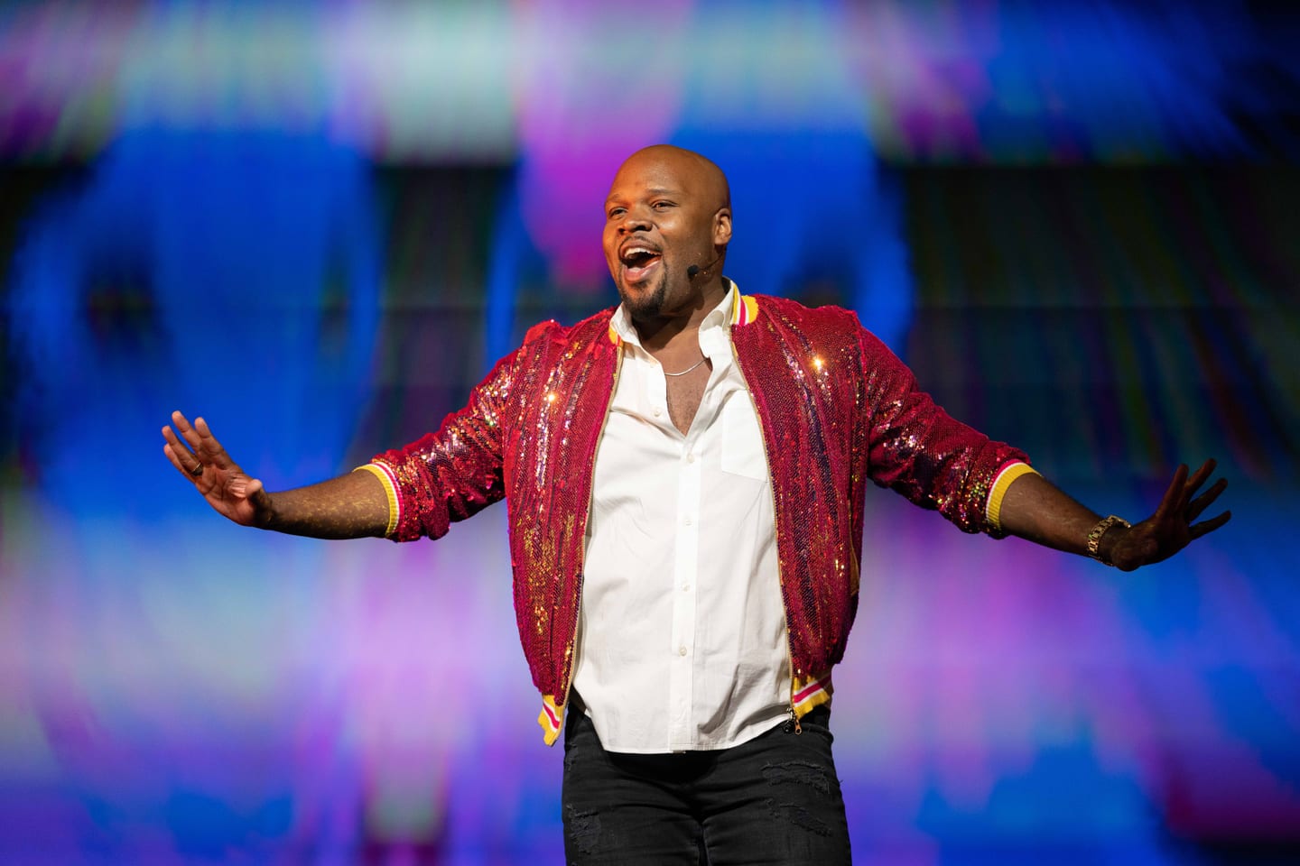 A vocalist in a red sequin jacket performing with arms outstretched on stage at the IPW travel trade show in Orlando