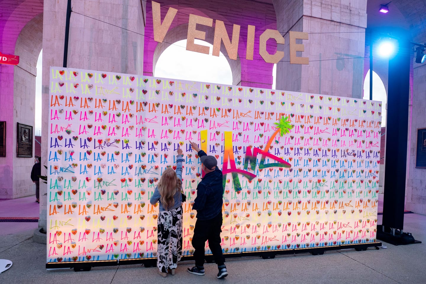 Guests pressing into a large pin-art interactive wall beneath a glowing VENICE sign at an IPW activation