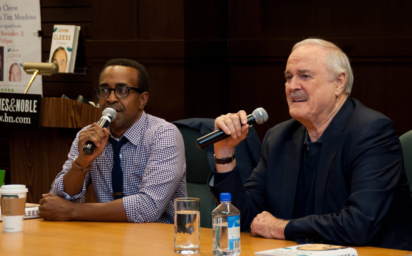 John Cleese and Tim Meadows each on a microphone in conversation at a Barnes & Noble author event