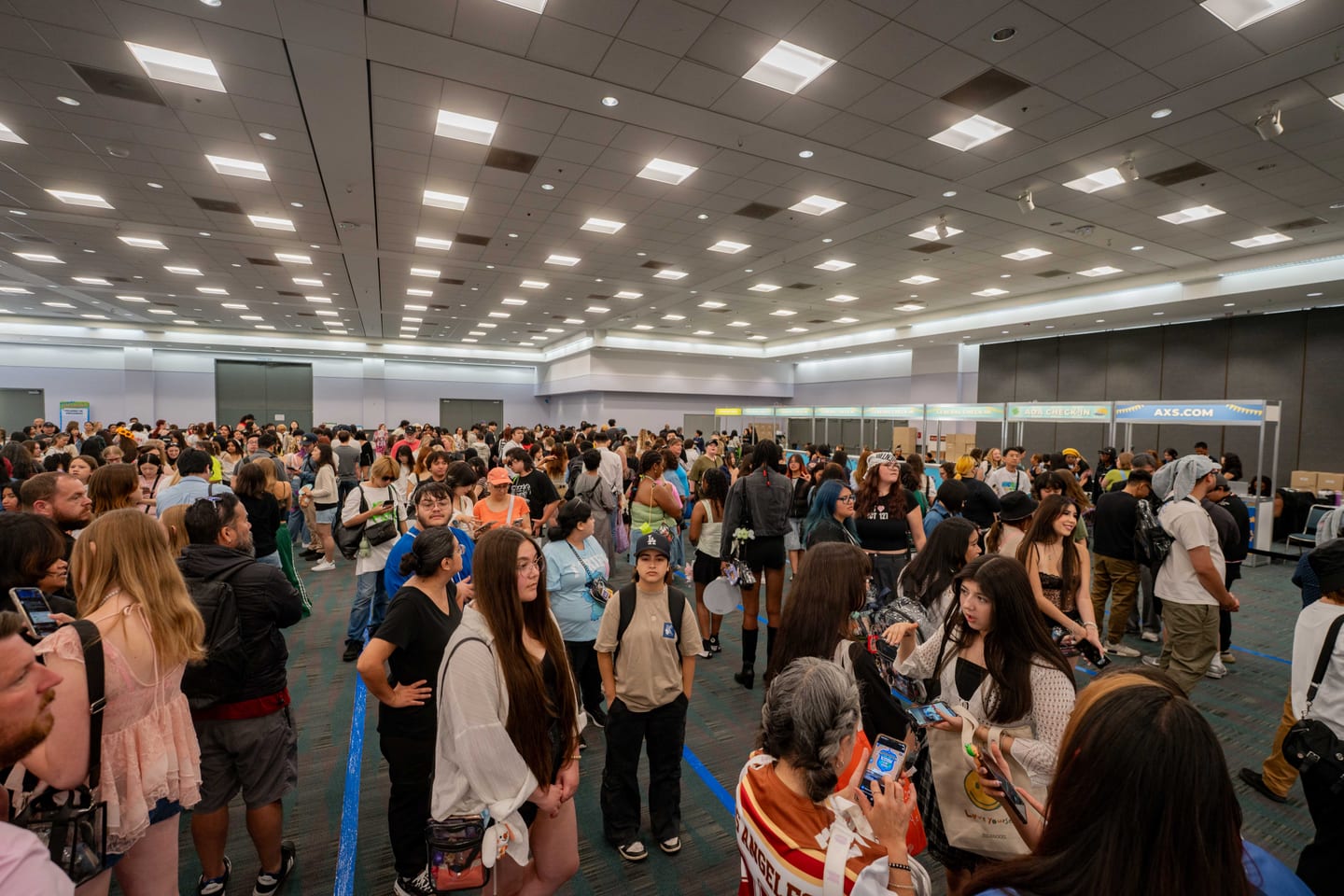 A packed KCON LA 2025 exhibit hall crowd filling the Los Angeles Convention Center floor beneath an AXS banner