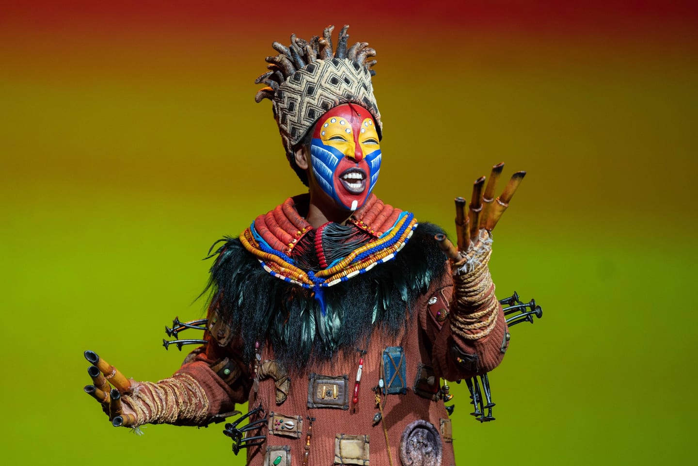 Theatrical performer in an elaborate Lion King-style costume under colored stage light